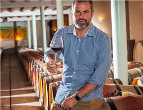 Portrait de Thierry THOMAS, le propriétaire du Mas du Novi, tenant un verre de vin rouge à la main
